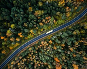 Arial view of heavy truck on a narrow twisting road. Autumn colorful trees by the sides of the road.